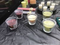 Multiple small votive candles in glass holders in red, yellow, and white colors displayed on black surface with black metallic holder visible.