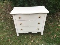 Front view showing the white-painted chest with 3 drawers and gold knobs.