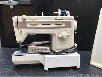 Side view of Finesse 834 sewing machine showing its stitch control dials, foot pedal attachment, and spool pin with blue thread.