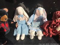 Photo showing two handmade bunny dolls in formal clothing and one Black Bear plush bear in plaid coat seated side by side.