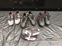 Three pairs of kids soccer shoes and one small baseball glove laid out on a black surface