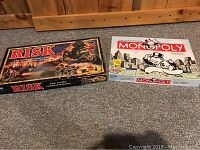 Photo showing both Risk and Monopoly boxed games side by side on carpet