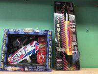 Photo showing remote control airplane boxed labeled 'Micro Jet' and model rocket labeled 'Hyper-X' side by side on a shelf.