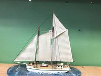 Ship art piece front view showing two large white sails, wooden hull, and plaster base designed to look like ocean waves.