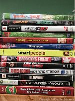 Photo of 13 DVDs with cases stacked vertically, showing titles including PlayStation 2 and Xbox 360 games, movies, and educational DVDs.