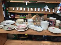 Front view of mixed cups and saucers with decorative floral and graphic designs on wooden shelf