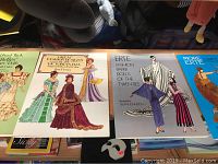 Four vintage fashion paper doll books arranged on a table, titles visible including Victorian era and Erte.