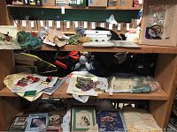 Overview photo showing shelves with assorted embroidery yarn skeins, embroidered pieces, patterns, and other materials.