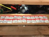 Full view of 22 cameo faces in original clear plastic packaging with red and white cardboard backing laid out in 2 rows on a wooden surface.