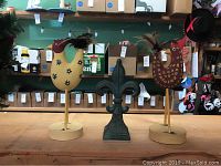 Three decorative figurines on wooden surface: one green metal fleur de lis in center and two wooden chickens with feather tails on either side.
