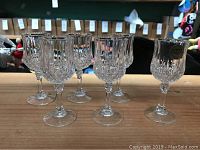 Set of six clear crystal cognac glasses with faceted design on the bowl and base, arranged on wooden surface.