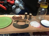 Various kitchen and household items arranged on a wooden surface including an herb chopper, plates, candlesticks, jar and doilies.