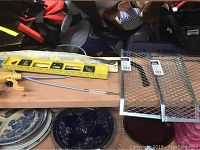 Wide view of yellow level, drain snake, metal grates, painting supplies and plates underneath