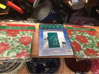 Photo showing two packaged holiday flannel table covers and one packaged dark green shower curtain set with hooks