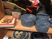 Shelf with various decorative tins including rectangular bear motif tin, round blue and white floral pattern tins, and a round tin with brick building illustration