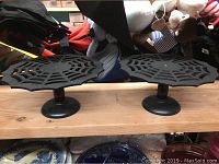 Two black wooden cupcake holders shaped like spider webs on pedestal bases, shown side by side on a wooden surface.