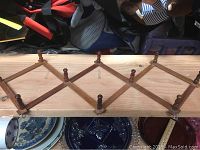 Wooden expandable peg rack on a wooden surface showing full rack with its diamond lattice structure and wooden pegs for hanging items.