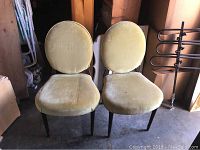 Pair of vintage wooden chairs with yellow fabric and oval backs showing stains on seats.