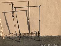 Full view of the black metal clothing rack with adjustable height, casting shadow on the wall behind.