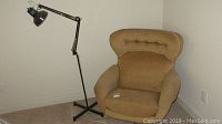 Tan swivel chair with stains beside adjustable black metal floor lamp