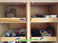 Photo showing wooden shelving unit with taped-off sections containing various cables, cords, small boxes, and stacked media such as CDs and VHS tapes.