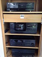 Four-tier wooden shelving unit holding audio components: top: Sansui D-950WR cassette deck; second tier: Pioneer PD-F906 CD player and storage unit; third tier: Yamaha RX-V590 receiver; bottom shelf: two Sonamp 260 speaker boxes.