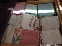 Drawer with folded kitchen linens including dish towels and pot holders in various pastel colors and patterns