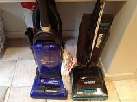 Photo showing both Hoover and Eureka vacuum cleaners side by side with a pack of vacuum bags in a laundry room.