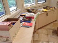 Counter with many soft cover books spread out and stacked, including boxed sets and binders visible.