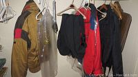Men's ski jackets and pants hanging in closet; brown and black Far West jacket with red accents visible.