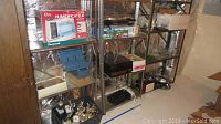 Shelving units containing all items including humidifier in box, record player, trophies, purses, tripod, and boxes.
