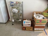 Wide view of wire shelf filled with canning jars and several cardboard boxes filled with additional jars and lids on the floor.