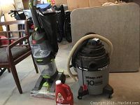 Garage setup showing the Hoover Dual PowerMax carpet washer, 10 gallon Shop-Vac, and gallon jug of Hoover carpet shampoo alongside chairs and boxes.