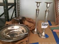 Wide shot showing two tall sterling silver candlesticks, a footed bowl, a serving bowl containing sterling flatware (knife, fork, spoon). All items monogrammed.