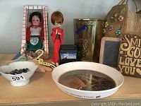 Wide view of all items showing dolls, bowl with marbles, wooden hangers, metal trash can, straw bag, plaque and chalkboard