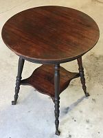 Full view of the antique two-tiered parlour table showing round wooden top, middle tier shelf, and turned legs.