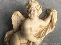 Front view of cream-colored cherub wall hanging on gray surface.