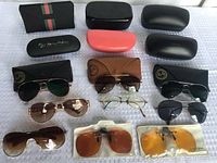 Photo showing all sunglasses and eyeglass cases arranged on white patterned surface, displaying brand logos and styles