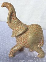 Side angle photo of cream and orange patterned elephant figurine, trunk raised, showing its right side and part of the front.