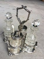 Front angle view of vintage condiment set on stand, showing four glass containers with two crystal stopper tops and one lid with a spoon.