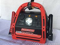 Front view of MotoMaster booster pack showing the control panel, LED light, positive and negative clamps.