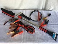 Photo showing two ice scrapers with attached brushes and jumper cables with copper clamps on a white textured surface.