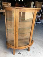 Front view of oak bowed glass display cabinet showing curved glass panels and door closed