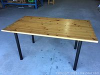 Full view of rectangular vintage pine wood dining table with black metal legs on concrete floor.