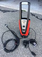 Front view of Husky electric power washer with hose coiled and spray trigger lying next to it, showing power switch and pressure dial on front panel