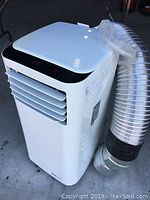 White UberHaus portable air conditioner front view with attached flexible silver exhaust hose. Black digital control panel on top.