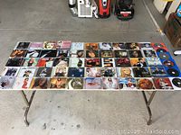 Top-down view of a table with over 50 music CDs in jewel cases spread out flat, showing album covers from various artists including Mariah Carey, Justin Bieber, Nicki Minaj, Michael Jackson and more.