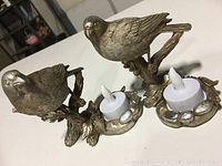 Two sparrow votive holders side by side on a white surface with LED tea lights inserted