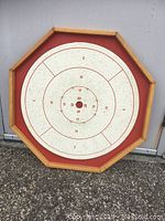 Front angled view of the vintage octagonal crokinole board with red and white scoring surface and wooden frame.