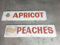 Front view of both vintage hand-painted nursery signs labeled APRICOT and PEACHES showing fruit graphics and orange text on white background.